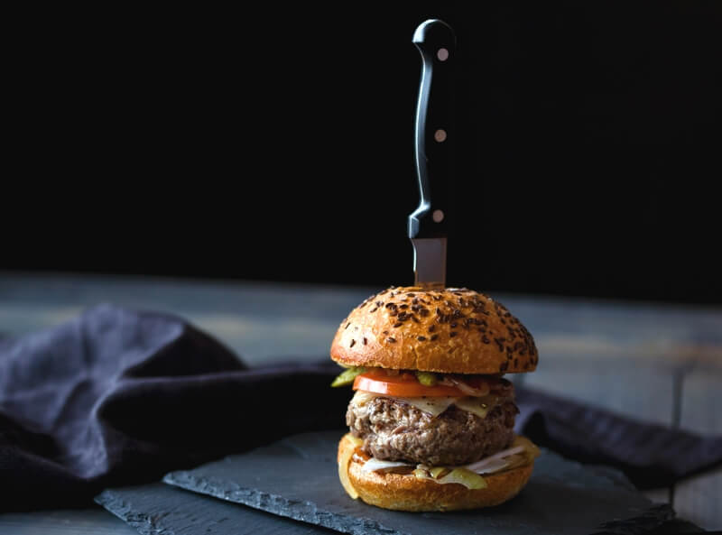 Delicious burger with knife stuck in top bun, food safety level 2 training.